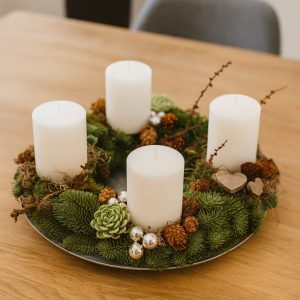 Adventskrans bundet af gran og hvide bloklys. Adventskransen står på et sofabord.
