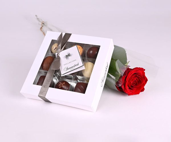 Chokoladeæske og en rød rose pakket i cellofan.