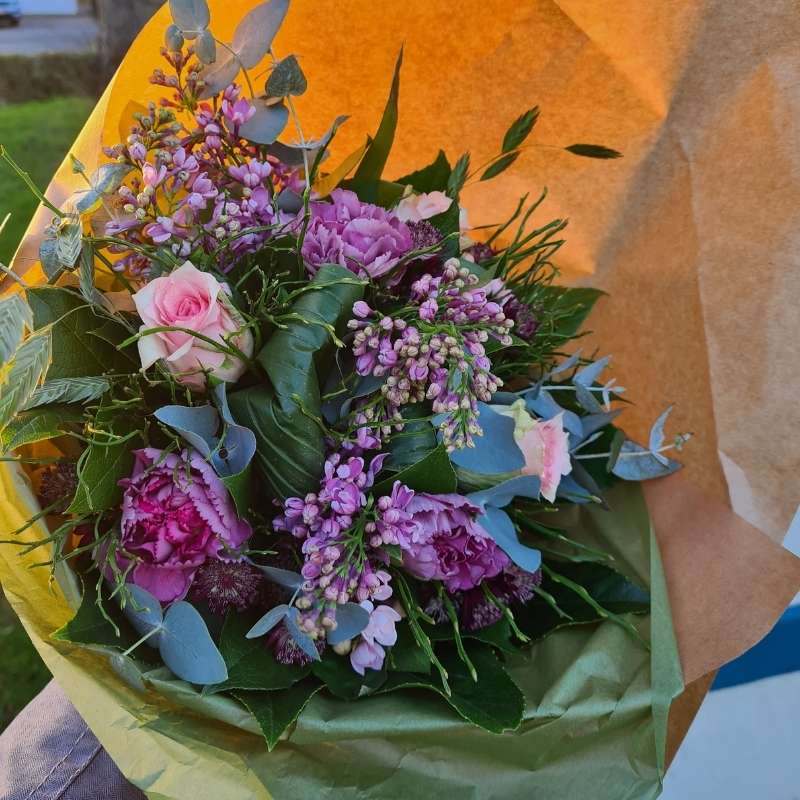 Buket i lilla og lyserøde farver med gerbera og nelliker, pakket ind til gave.