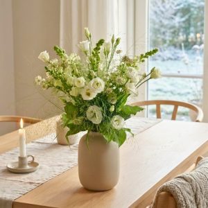 Hvid buket står i en keramikvase på et spisebord.