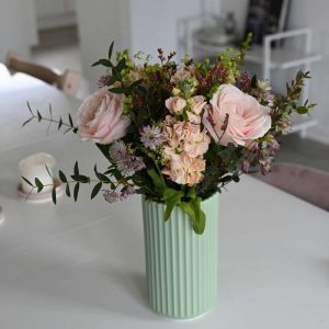 Buket med lyserøde roser, og andre lyserøde blomster som astrantia, limolium, leukøjer og forskelligt grønt på hvidt bord