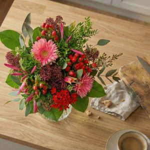 Buket i rødlige nuancer står på et træbord.