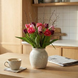 En smuk buket blandede tulipaner med forårsgrene, står på et bord i et køkken.