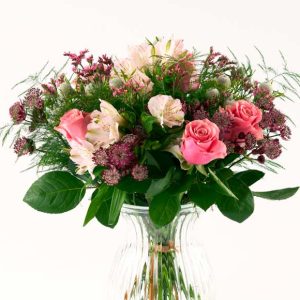 Luftig buket i rosa nuancer, som står i en gennemsigtig glasvase.