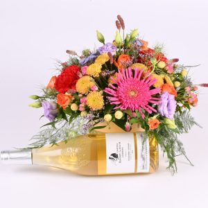 Friske blomster i en rund æske, og foran dekorationen ligger der en flaske vin.