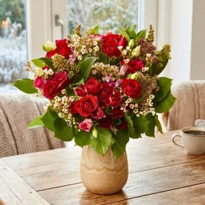 En buket i rød og hvid står i en keramikvase på et spisebord.