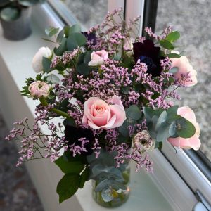 Luftig buket i rosa og lyserøde nuancer, som står i en gennemsigtig glasvase i en vindueskarm.