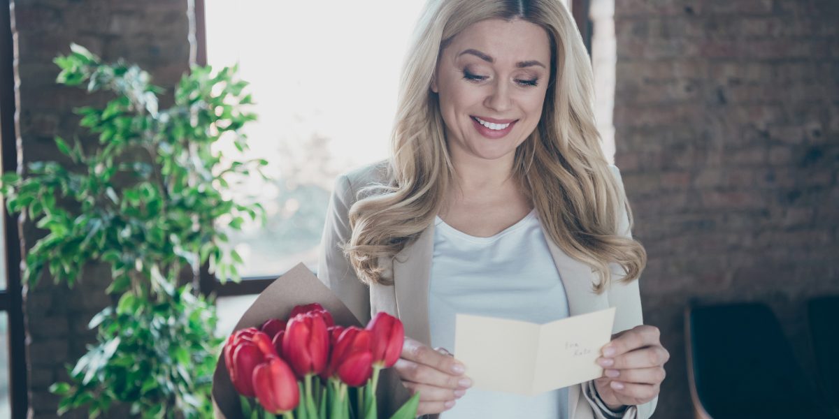 Kvinde står og læser et kort ved siden af en buket røde tulipaner i en vase.