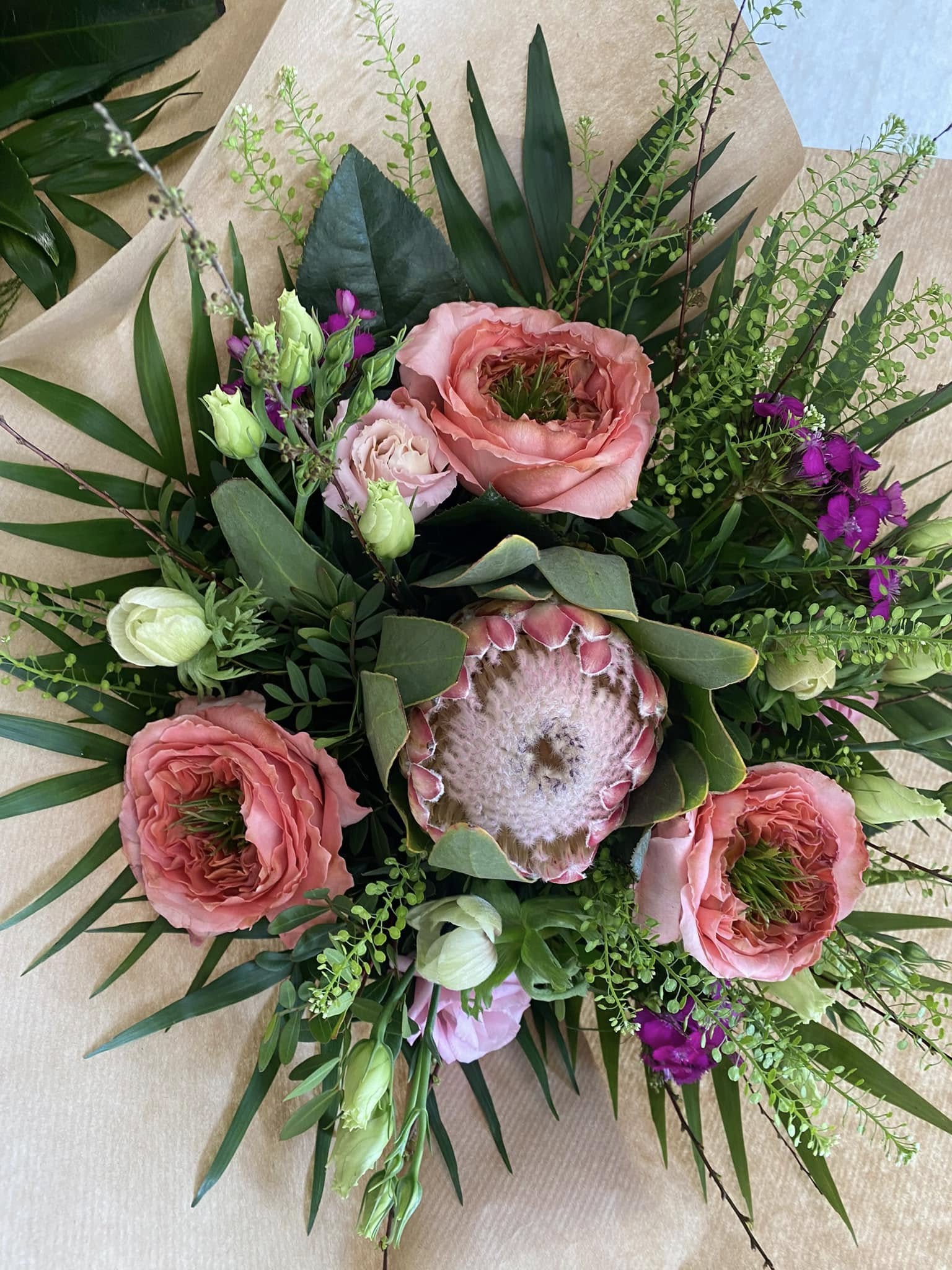 En buket fotograferet oppefra. BUketten indeholder rosa blomster og buketten er pakket ind i brunt papir.