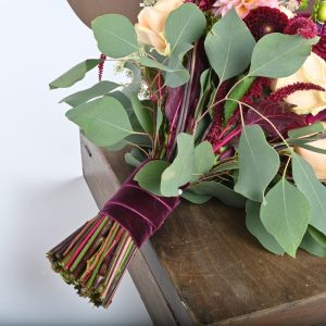 Brudebuket af georginer og riser i fersken og bordeaux farver hvor håndtaget er synligt med et bordeauxfarvet silkebånd.