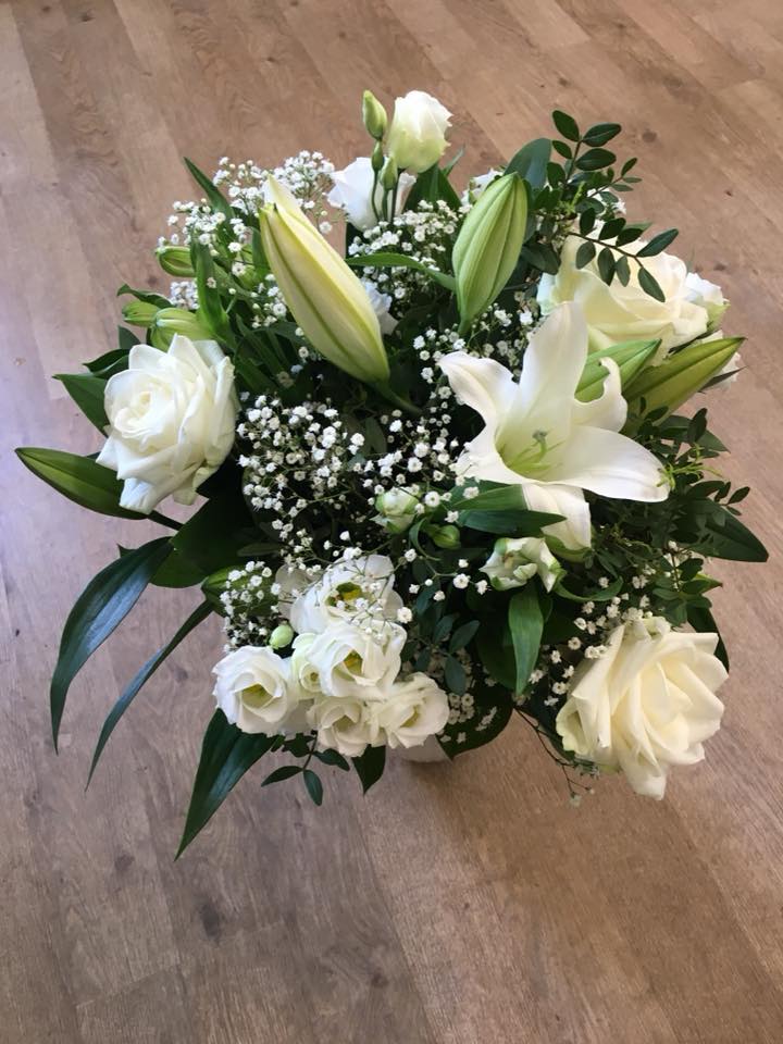 En hvid buket fotograferet i fugleperspektiv. Buketten indeholder hvide liljer, roser, brudeslør og santini chrysanthemum.