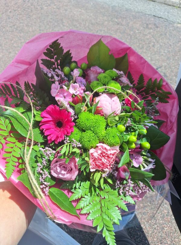 EN pink og grøn buket pakket ind i silkepapir.