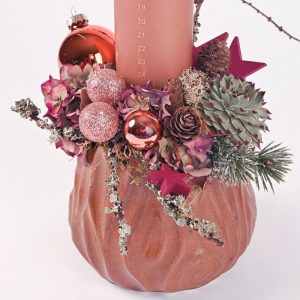 Nærbillede af rosafarvet kalenderlys med guldtal placeret i en keramikkrukke som er pyntet fint til en juledekoration.