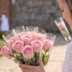 Konfirmand står med enkeltindpakkede, lyserøde roser.