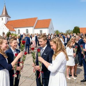 Konfirmander står foran kirken med hver sin røde rose