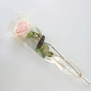 Lyserød langstilket rose indpakket i cellofan med Bloomit klistermærke på.