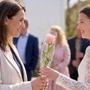 Lyserød rose overrækkes fra en kvinde til en konfirmand.