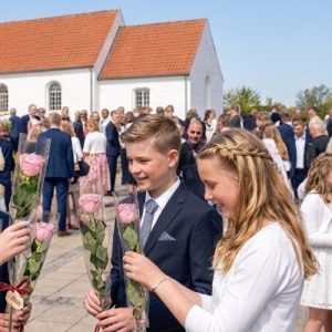Konfirmander står foran kirken med hver sin lyserøde rose