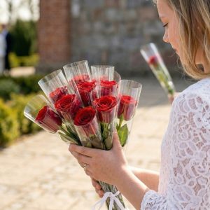 Konfirmand står med enkeltindpakkede, røde roser.