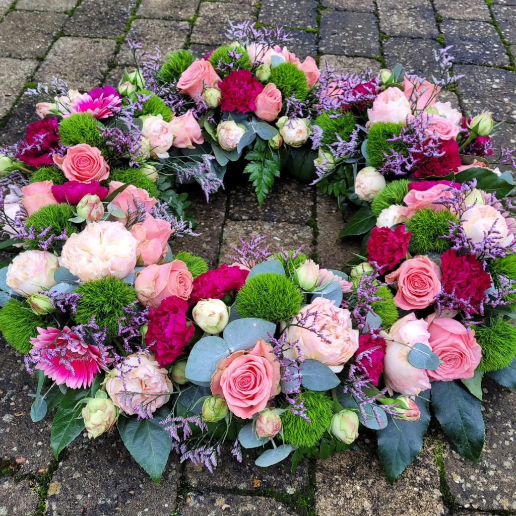 Begravelseskrans i rød, lyserød og lilla blomster.