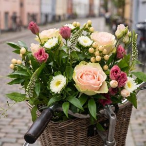 En buket i rosa, hvid og creme, står indpakket i en cykelkurv.