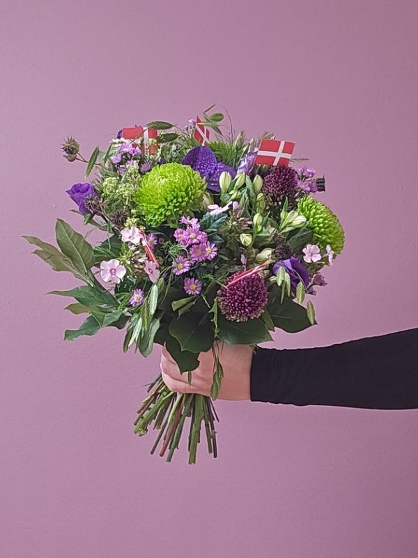 Lilla og grøn buket holdes frem foran en væg.