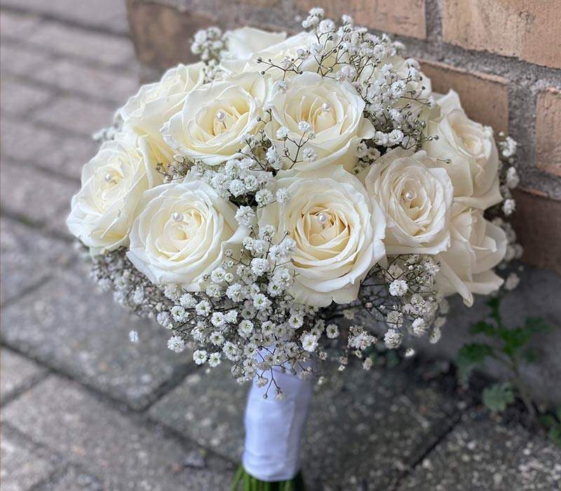 Rund brudebuket bundet af hvide roser og brudeslør.