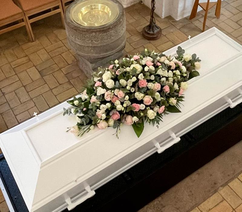 Kistepynt placeret på en kiste i en kirke. Kistepynten er bundet af hvide og lyserøde roser.