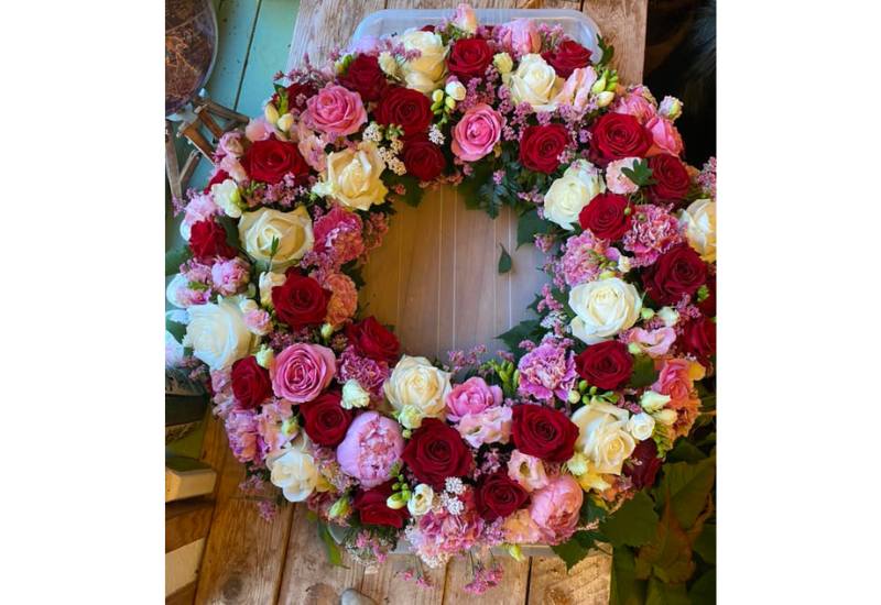 Begravelseskrans i hvide, lyserøde og røde farver af bl.a. roser, bonderoser, fresia og nelliker.