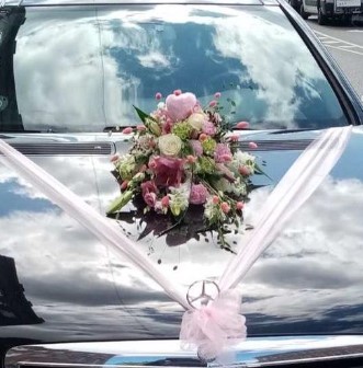 En bil, der er pyntet med en flot blomsterdekoration i hvide og lyserøde farver.